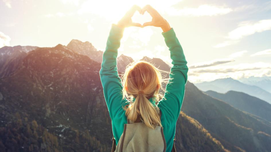 person on a mountain holding their hands over their head in the shape of a heart