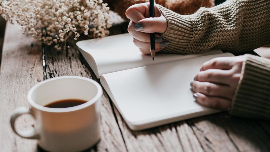 person writing in a journal with a cup of tea
