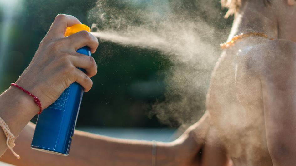 person spraying suncreen on a childs' back