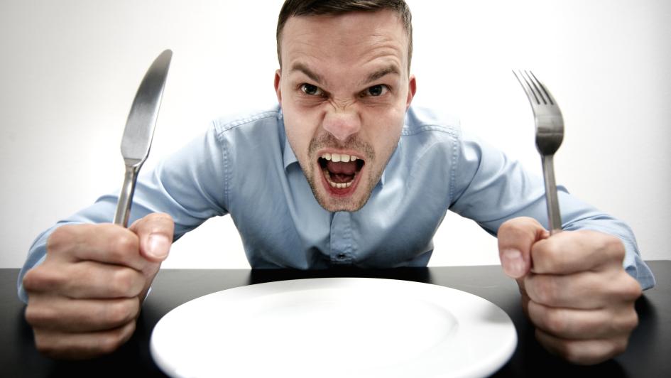 person with a fork and kinfe beside empty plate on table looking angry