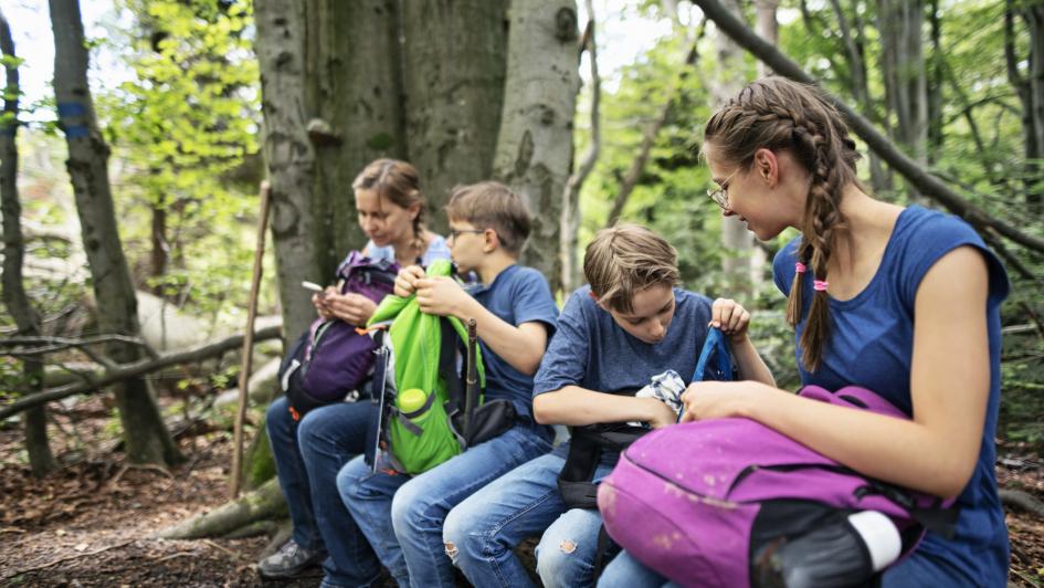 family of four grabbing food from their bags sitting on a log