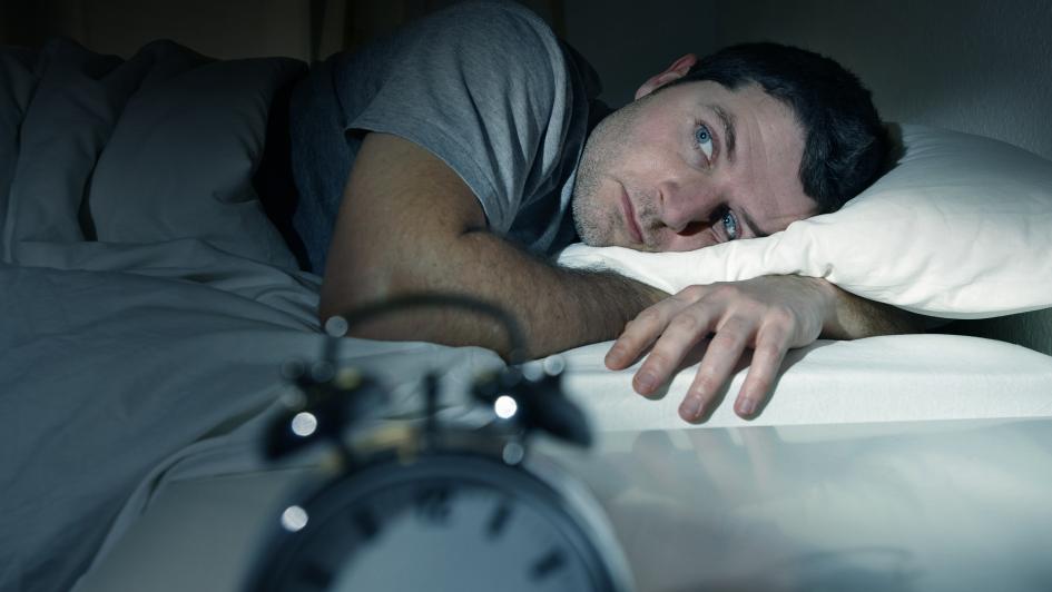 person laying in bed awake looking at alarm clock