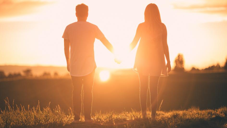 two people holding hands walking toward the sunset