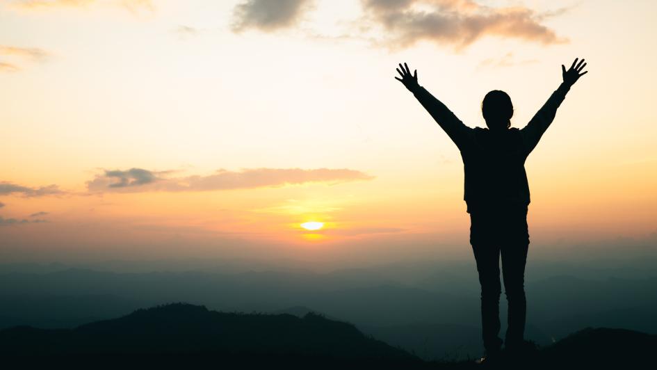 woman standing at the top of a mountain overlooking a sunrise